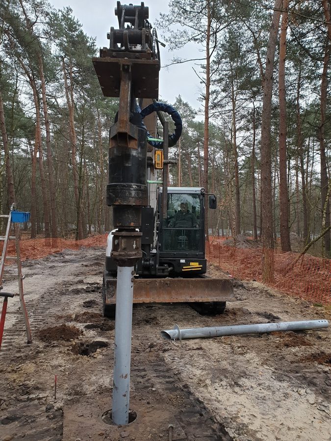 Excavator installing galvanized helical screw pile among pine trees at Bosland forest, Belgium