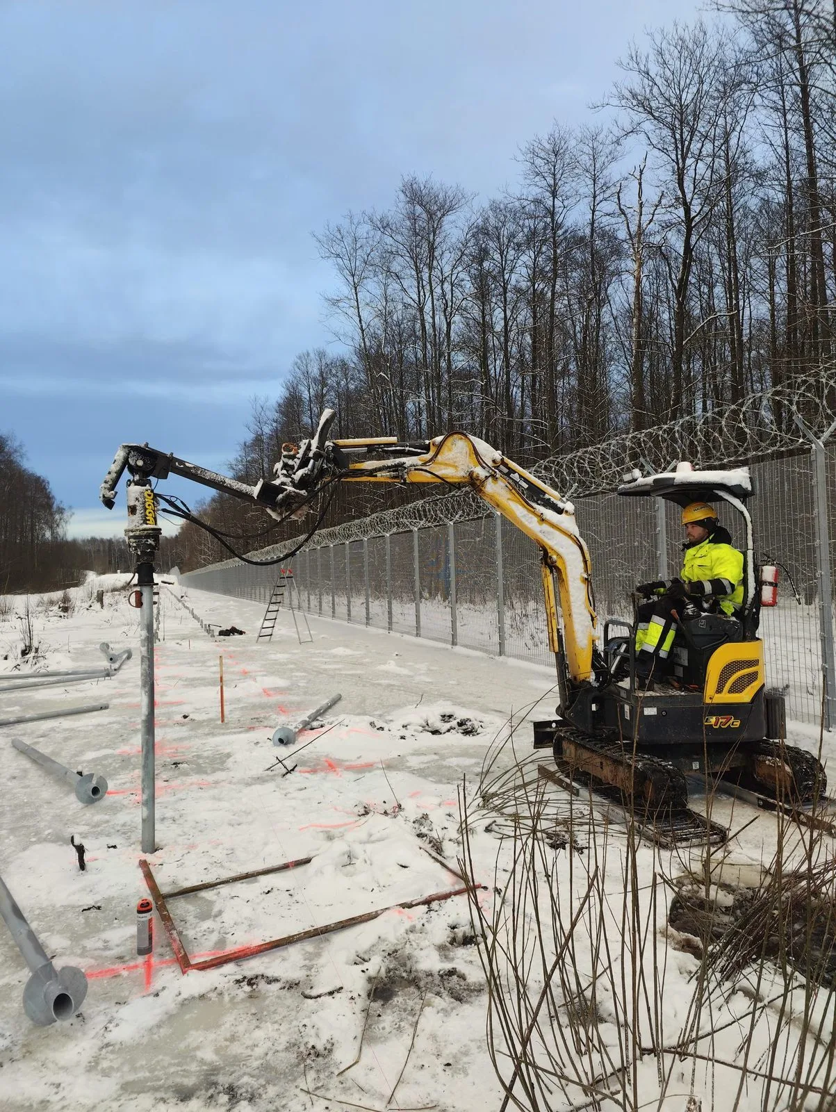 Mini excavator installing a screw pile in frozen ground