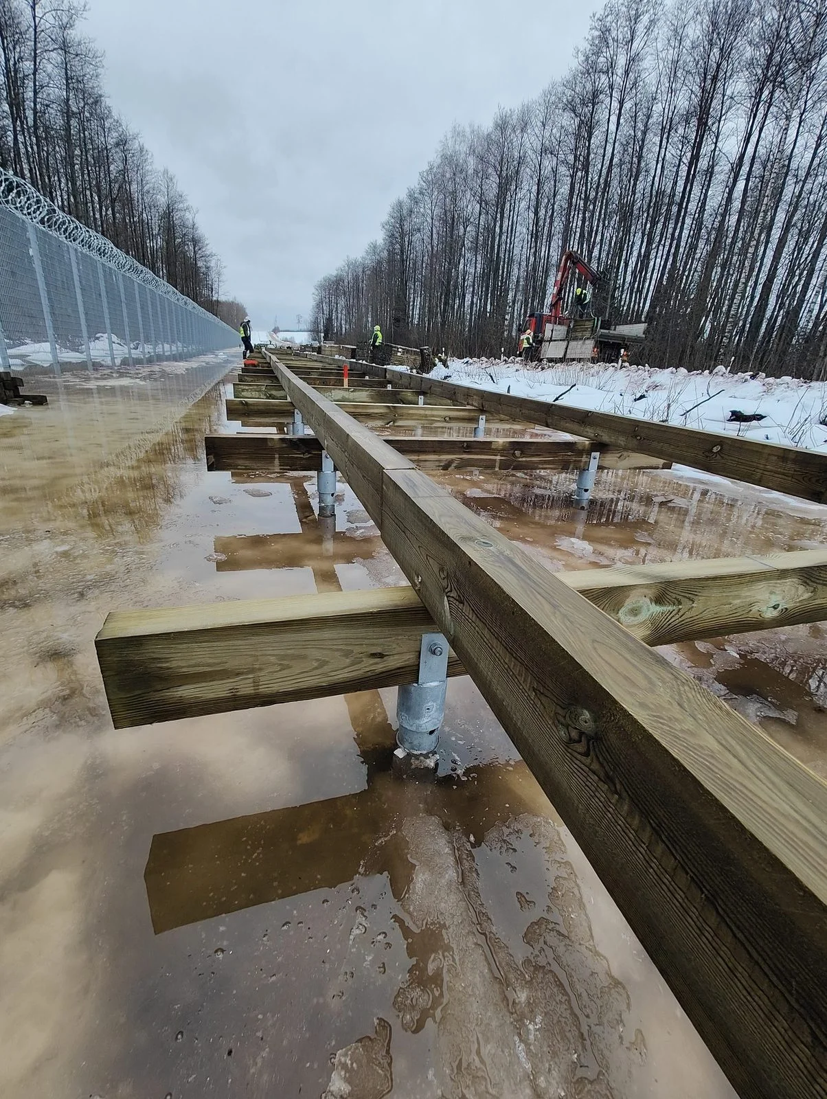 Wooden walkway frame mounted on screw pile U-brackets during Latvia border boardwalk construction