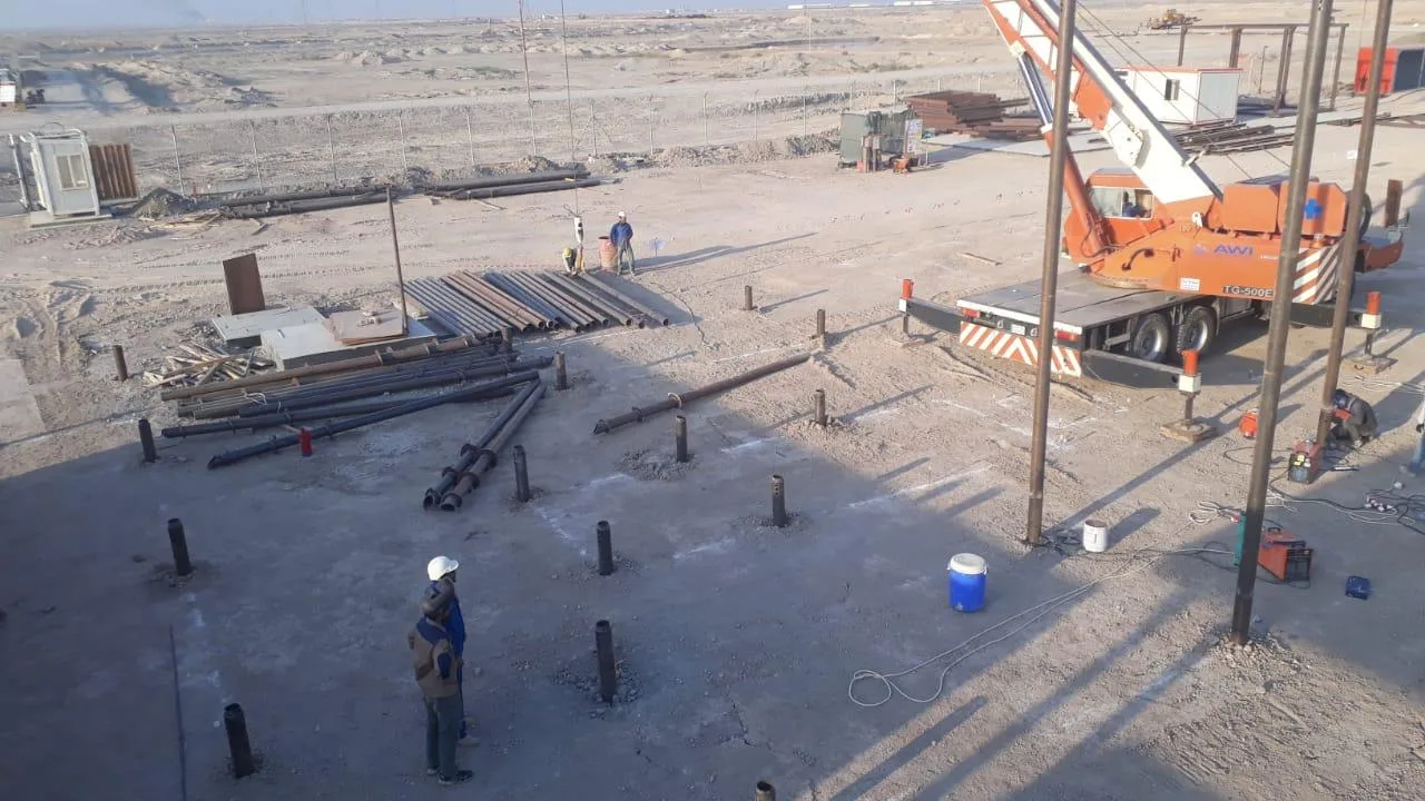 Screw pile installation with crane on Basra oil field, workers positioning helical piles in desert conditions